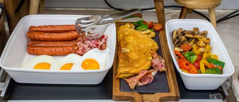 Un bufé de desayuno con salchichas, huevos, una tortilla y un plato de verduras.