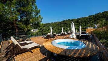 Eine Holzterrasse mit Whirlpool, Liegestühlen und Sonnenschirmen.