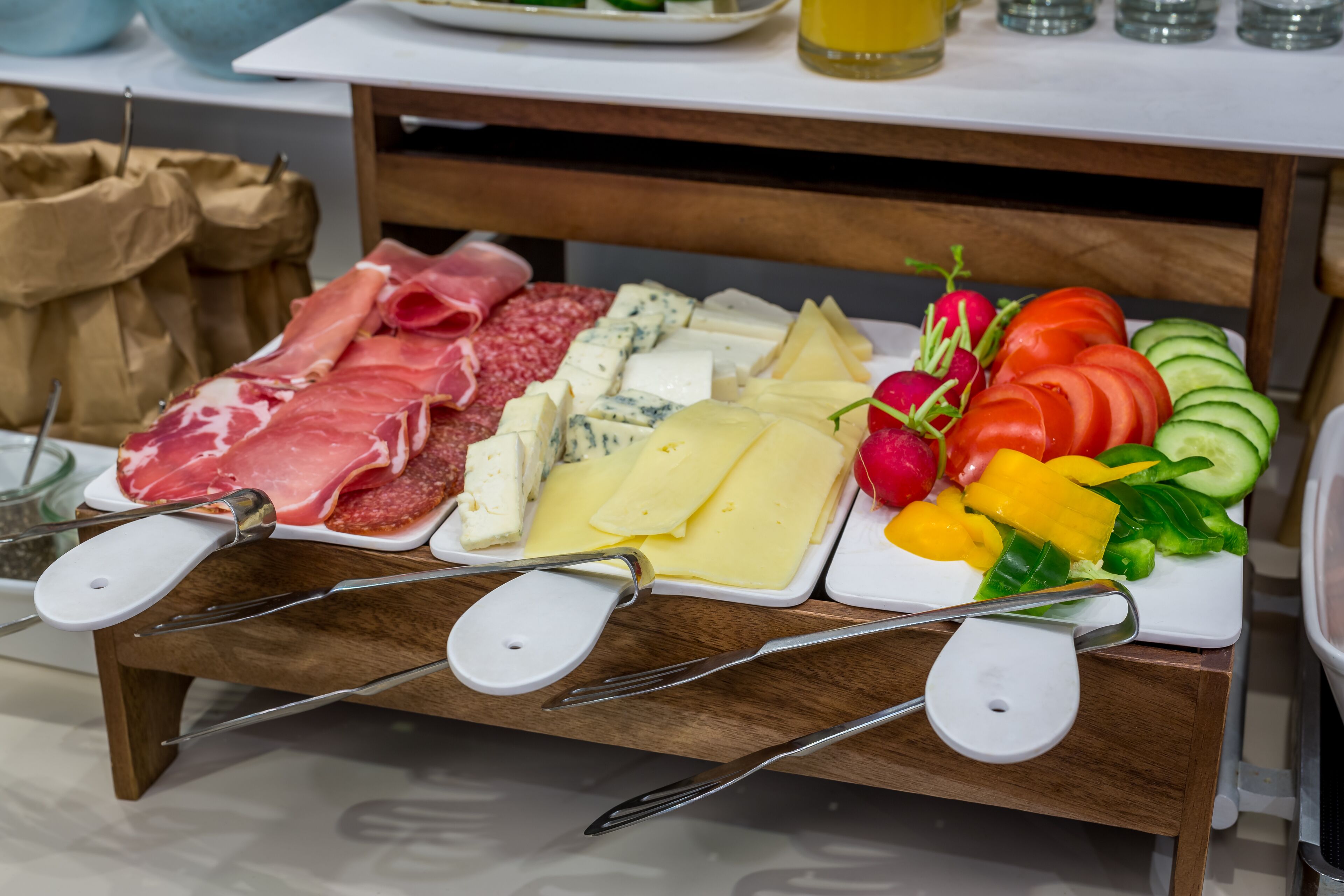 A wooden board with various cheeses, cured meats, and fresh vegetables.
