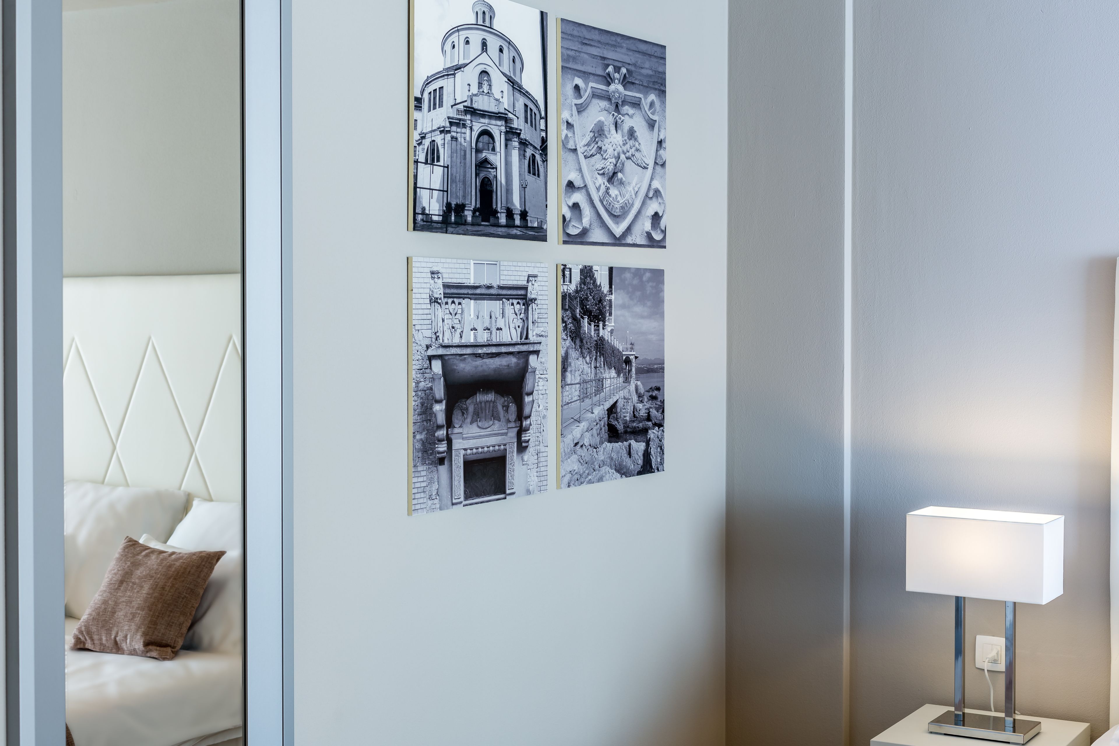 Un mur orné de quatre photographies en noir et blanc, un canapé blanc avec un coussin marron et une lampe de table au design moderne.