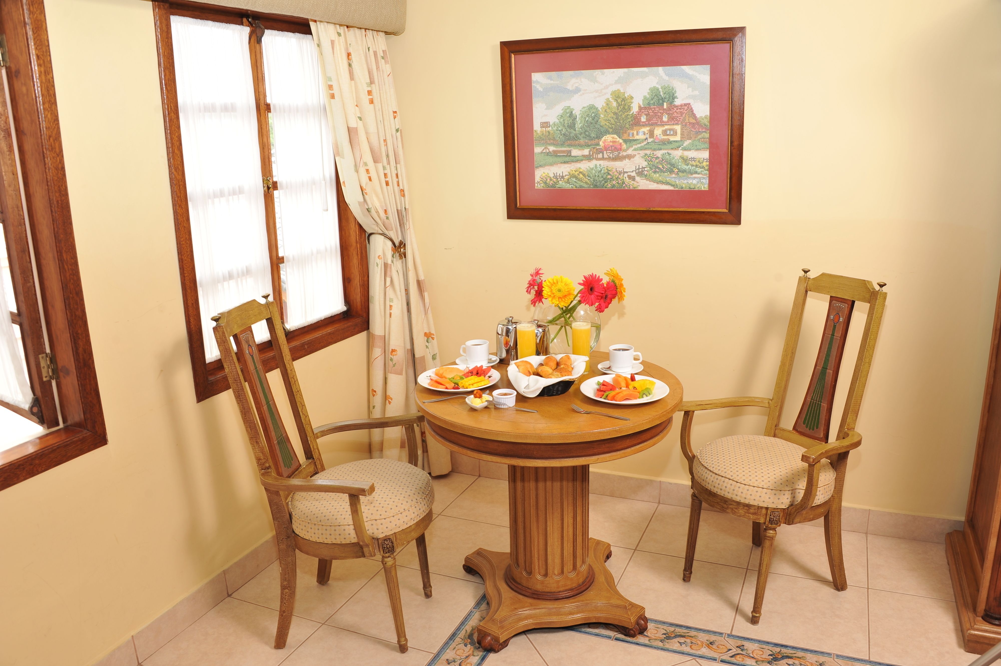 A dining area with a round wooden table, two chairs, and a painting on the wall.