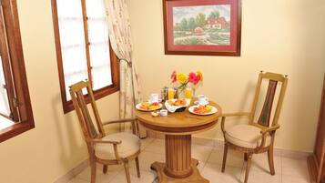 A dining area with a round wooden table, two chairs, and a painting on the wall.