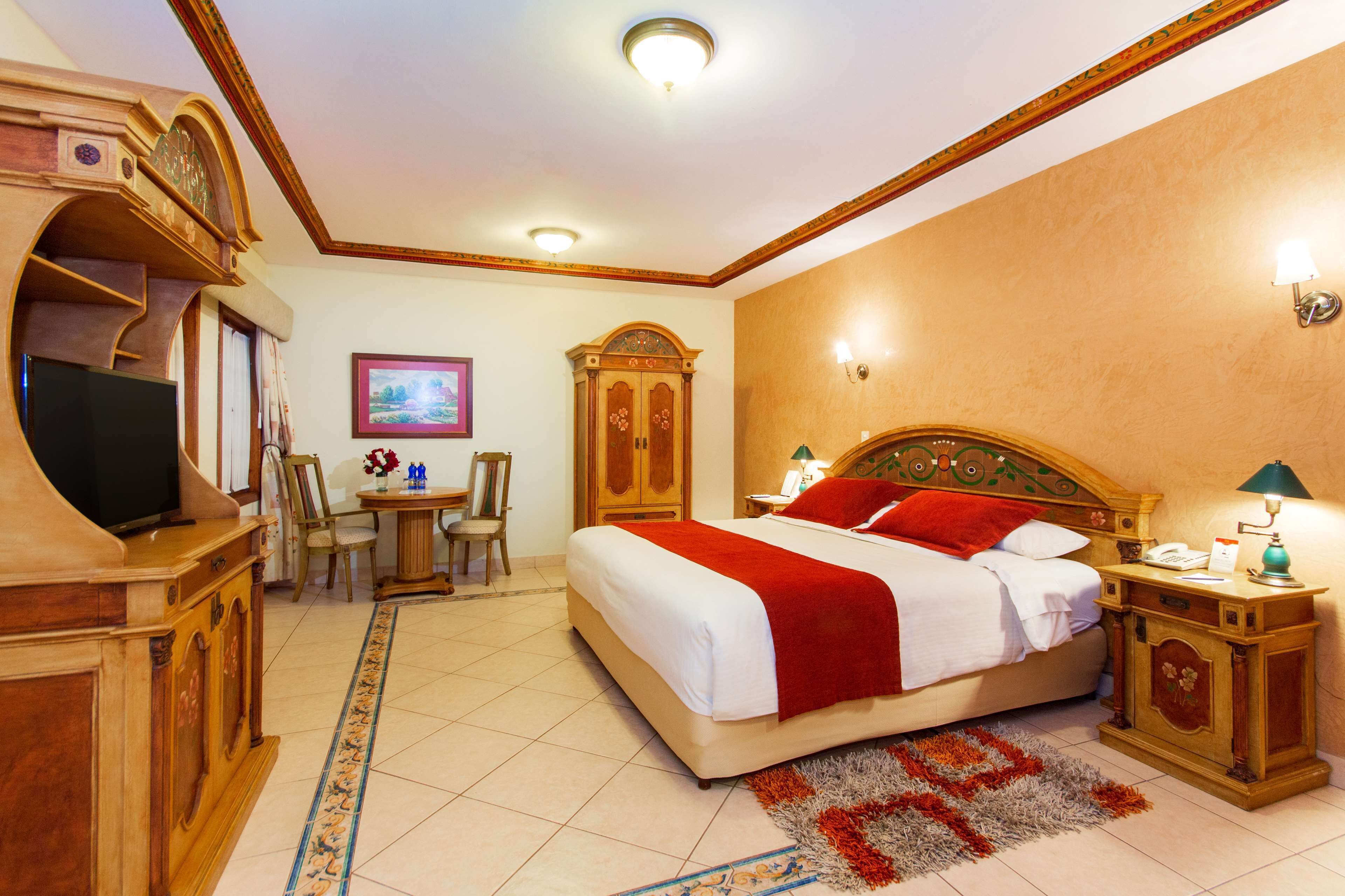 A hotel room with a large bed, a desk with a chair, a television, and a wardrobe.