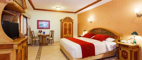 A hotel room with a large bed, a desk with a chair, a television, and a wardrobe.