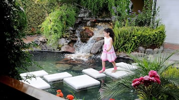 Stroll through the serene garden, featuring a small waterfall and stepping stones leading to a tranquil pond surrounded by lush plants and flowers.