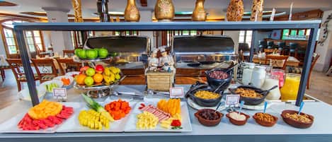 A buffet with various food items and a kitchen area in the background.