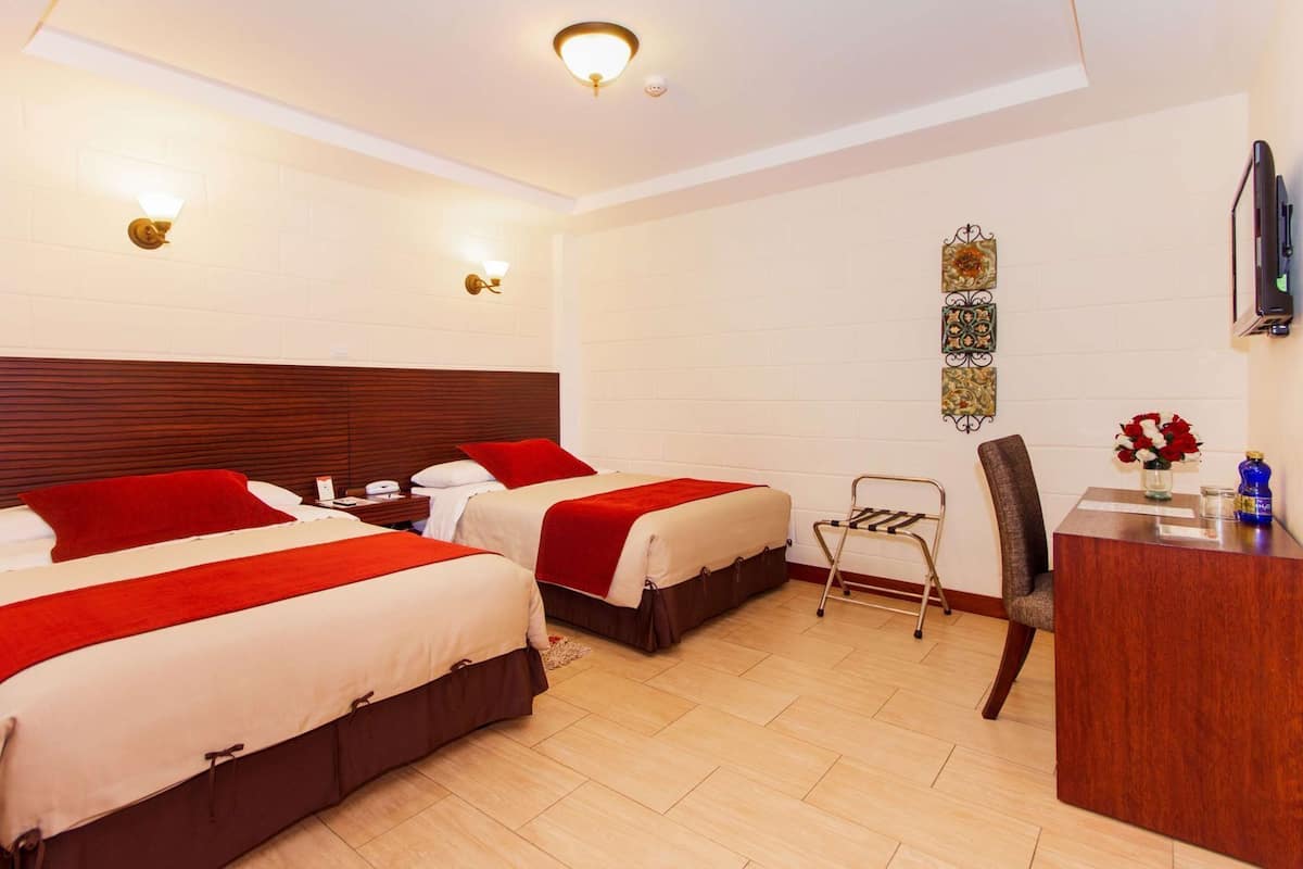 A hotel room with two beds, a desk, a chair, a small table, a TV, and decorative wall art.