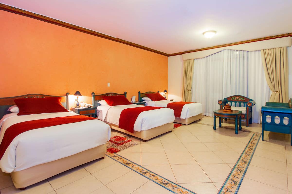 A hotel room with two beds, a small table, a chair, and a nightstand with lamps.