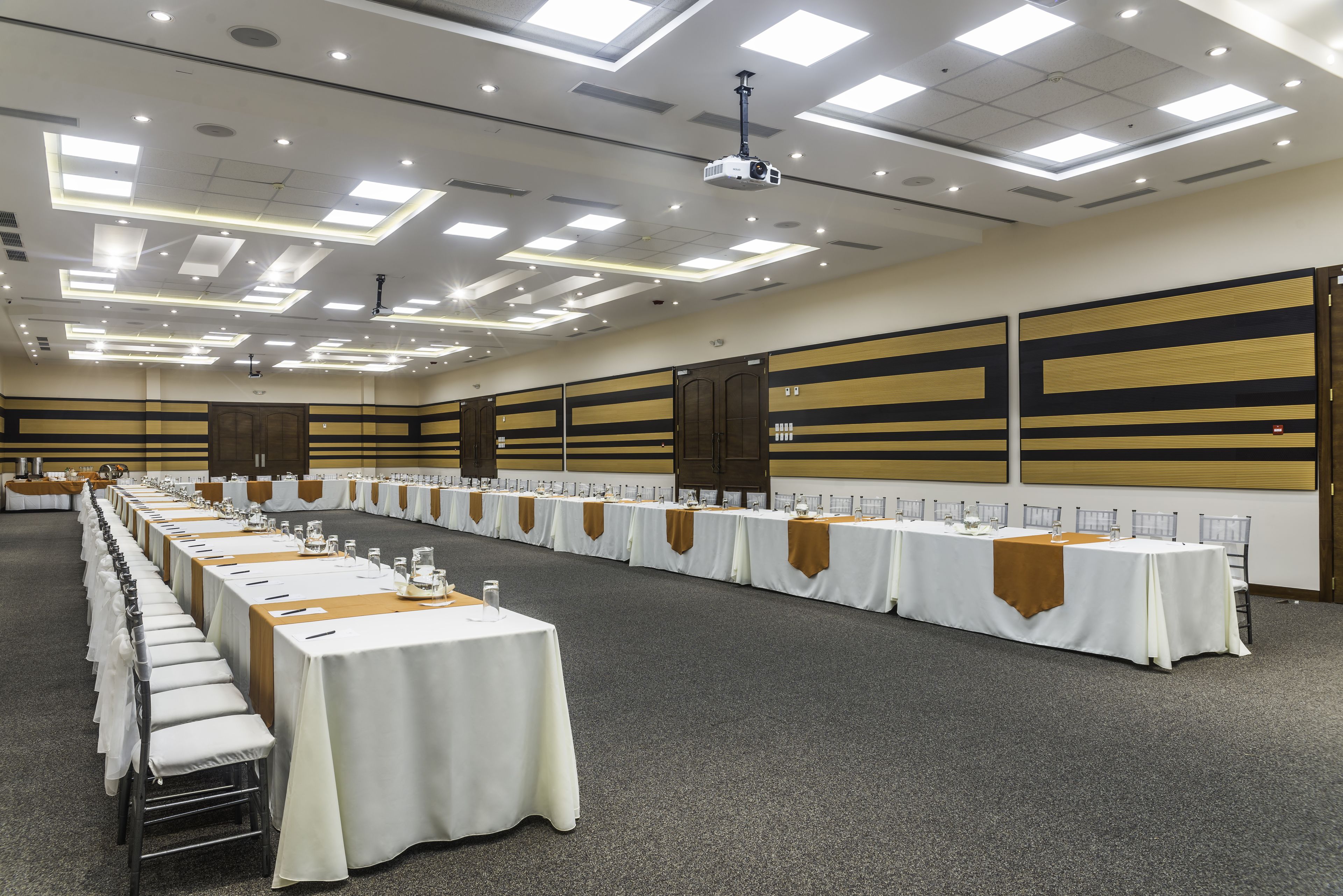 A conference room with long tables, chairs, and a projector on the ceiling.