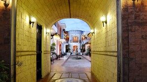 A corridor with a tiled floor leading to a central fountain, flanked by walls with light fixtures and potted plants. - Hotel Rincon de Puembo, BW Signature Collection (Puembo)