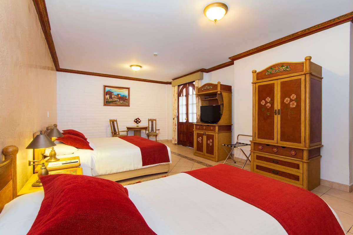 A hotel room with two beds, a wooden wardrobe, a television, and a painting on the wall.