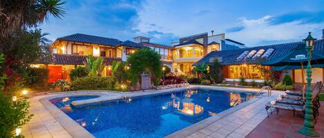 A swimming pool surrounded by a well-maintained garden and a building with multiple balconies.
