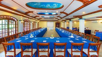 Un salón de conferencias con una larga mesa dispuesta para una reunión, sillas de madera y una pantalla grande al frente.