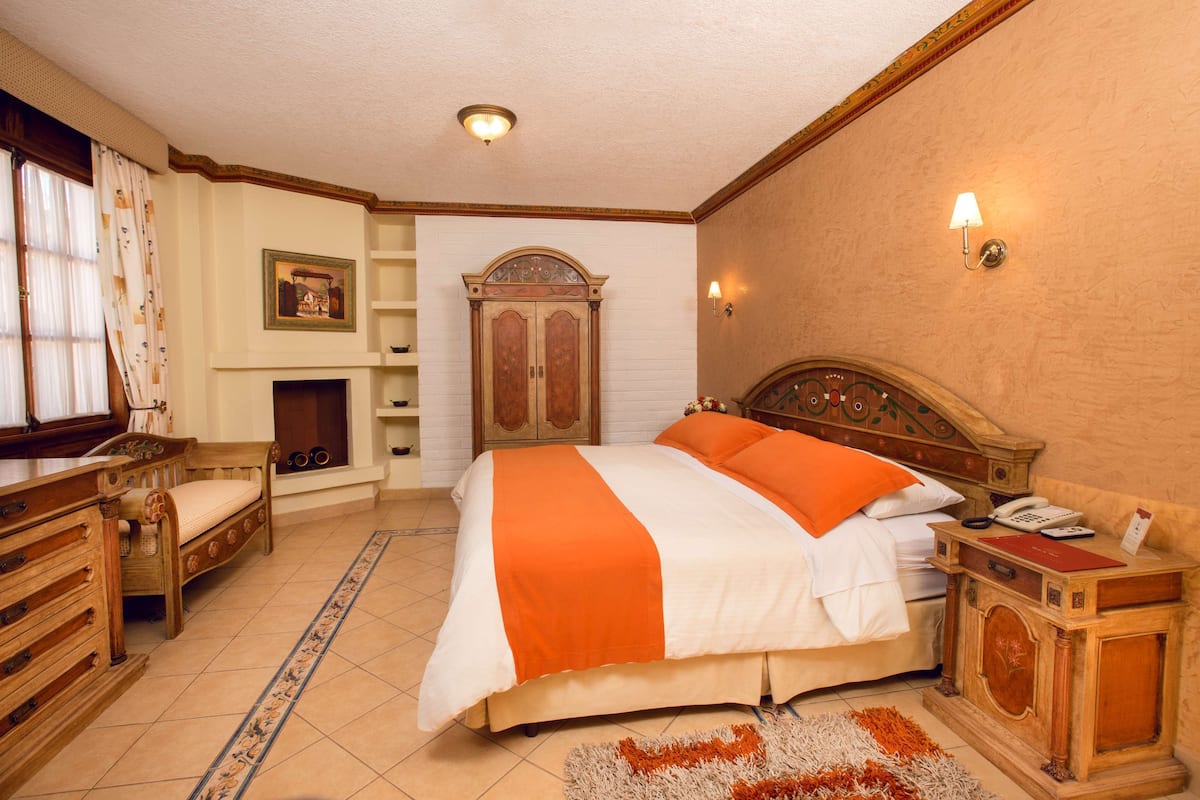 A hotel room with a large bed, wooden furniture, a fireplace, and a nightstand with a phone.
