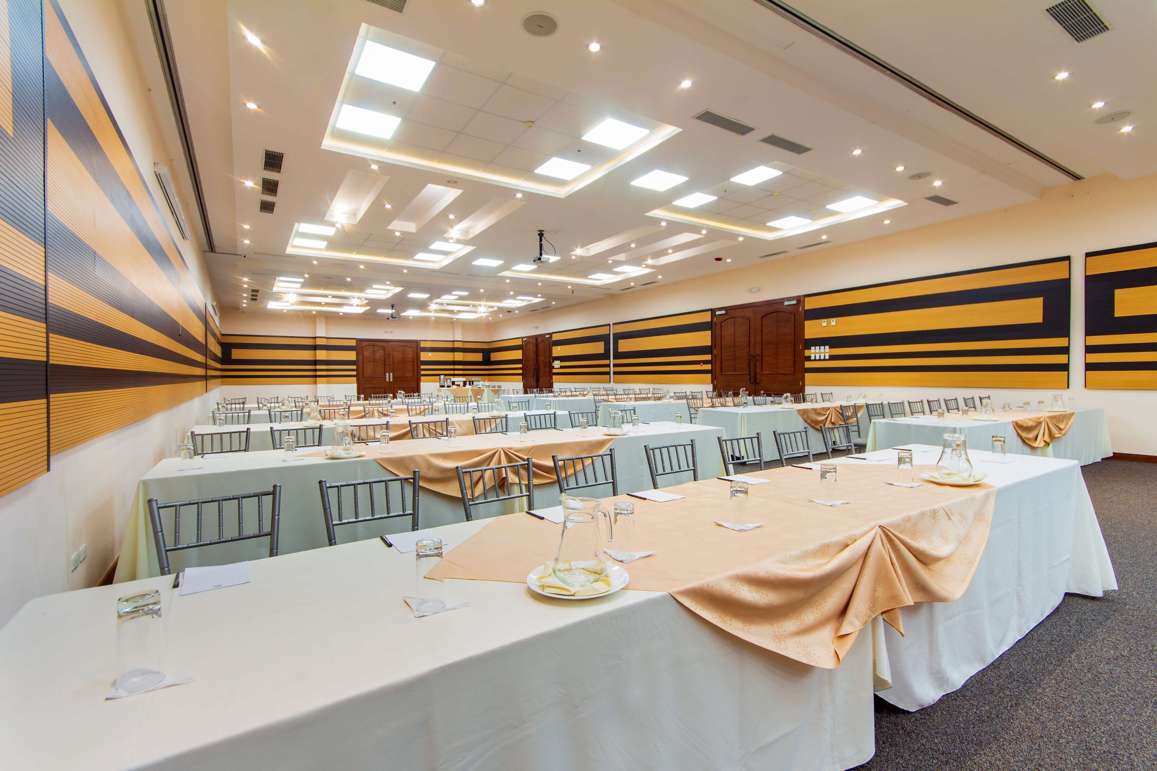 Un salón de conferencias con varias mesas, sillas y un techo alto con iluminación empotrada.