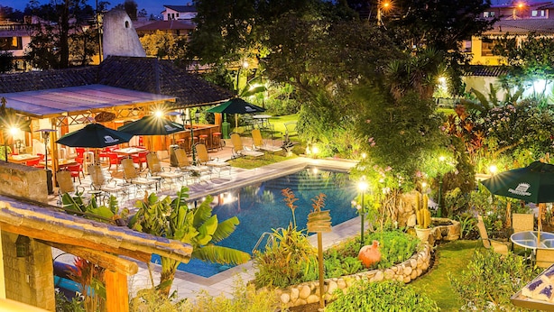 A pool area with lounge chairs and umbrellas, surrounded by lush greenery and a stone wall. - Hotel Rincon de Puembo, BW Signature Collection (Puembo)