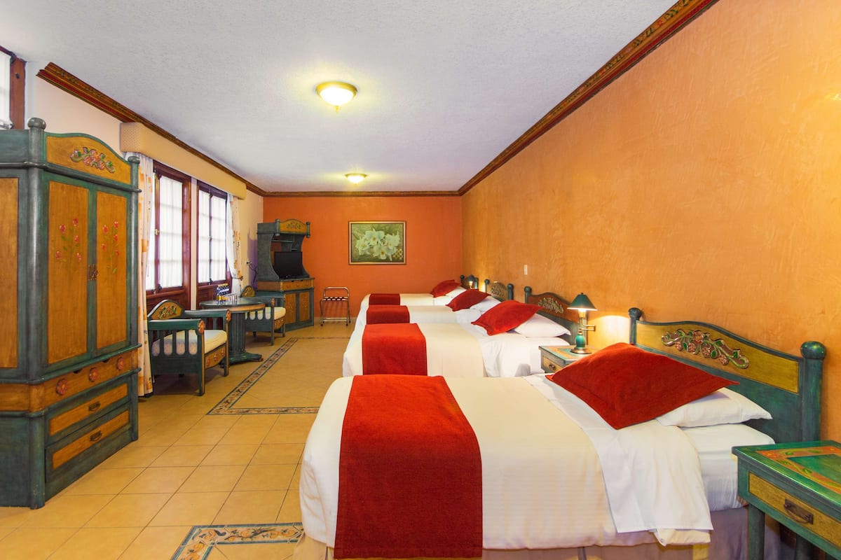 A hotel room with two beds, a wooden wardrobe, a small table, and a painting on the wall.