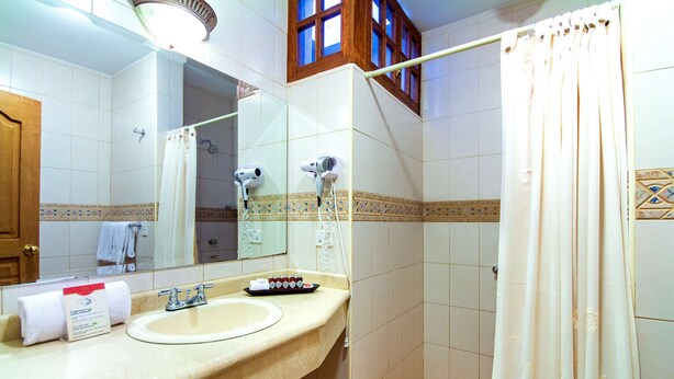 Une salle de bain équipée d’un lavabo, de deux sèche-cheveux, d’un porte-serviettes et d’un rideau de douche.