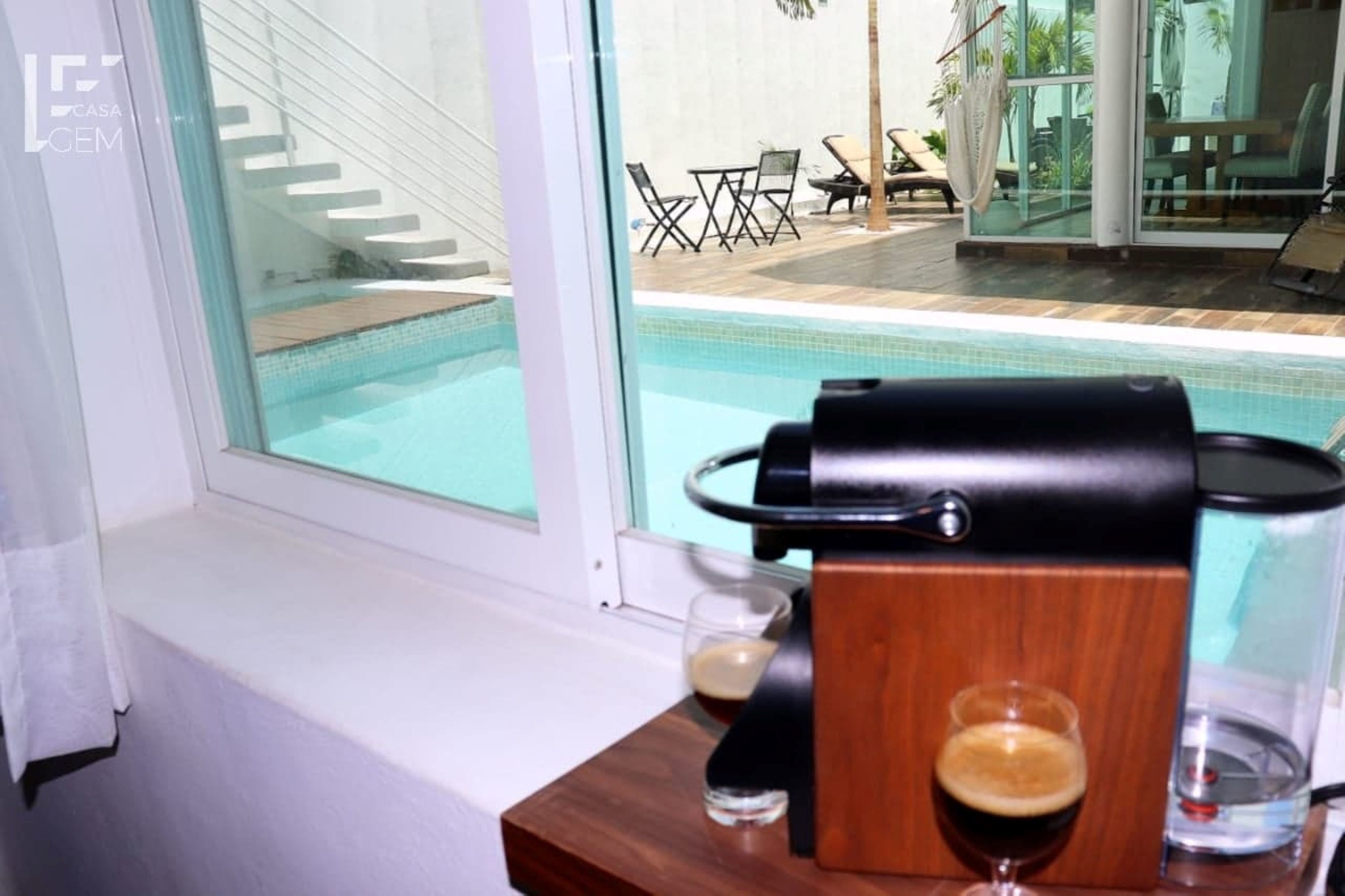 A poolside area with a grill, two glasses of beer, and a view of the pool and outdoor seating.