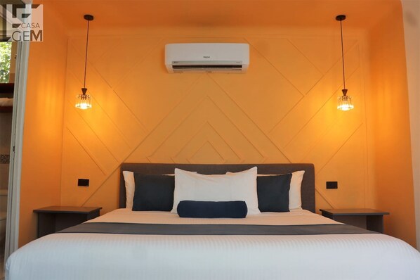 Habitación de hotel con cama, dos mesitas de noche, unidad de aire acondicionado y lámparas colgantes.