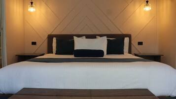 A hotel room with a large bed, two bedside tables, a wooden bench, and two pendant lights.
