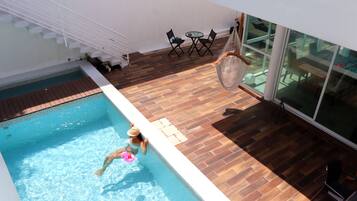 A swimming pool with a person in the water, a wooden deck, a glass table, and chairs.