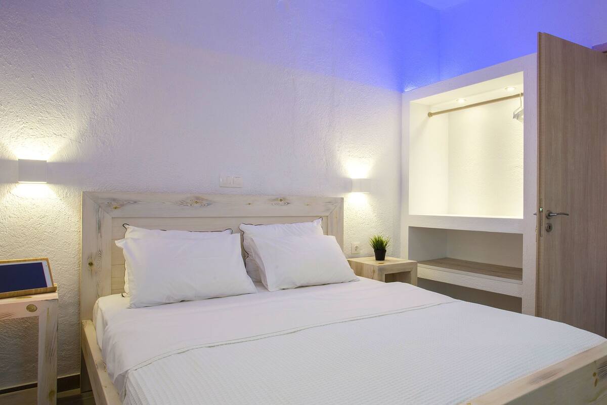 A neatly made bed with white linens, a wooden headboard, bedside tables with lamps, and a small potted plant.