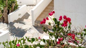 A white building with a stone staircase leading to a balcony overlooking a beach and the sea. - Pahivouni Studios & Suites (Naxos)
