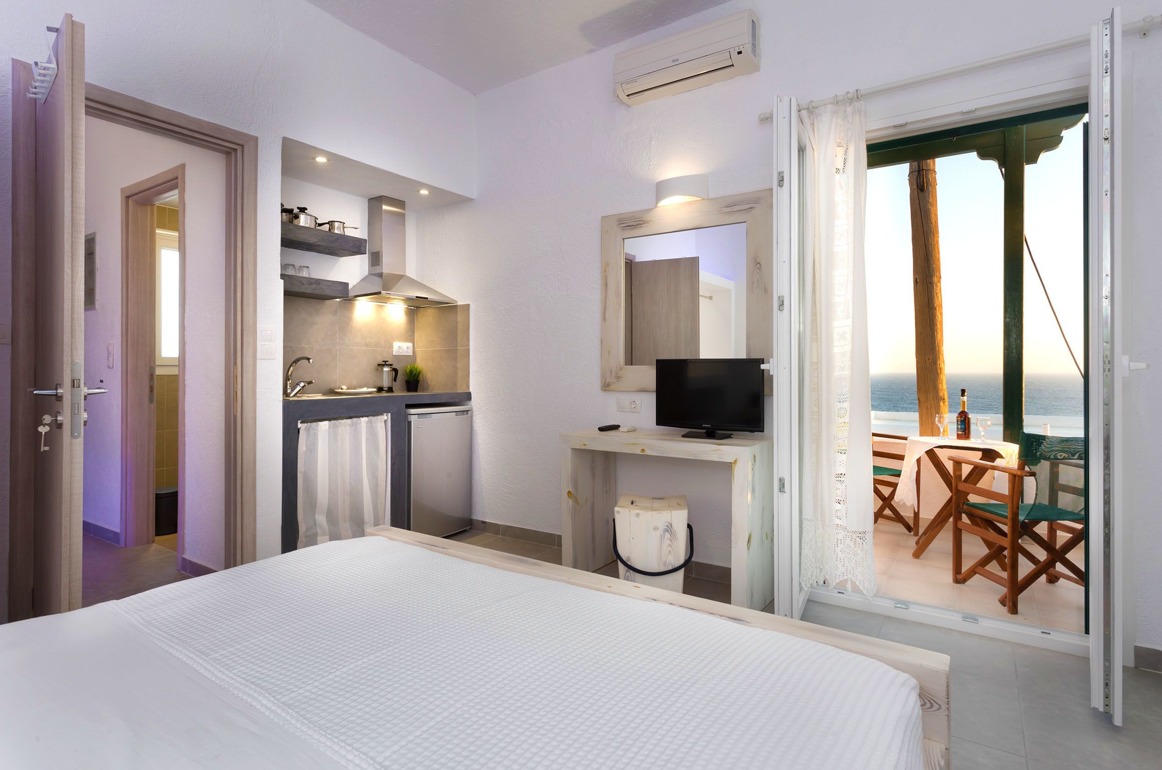 A hotel room with a bed, kitchenette, TV, and a balcony with a table and chairs.