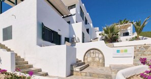 A white building with a stone entrance, a sign for 'Pahivouni Studios & Suites,' and a staircase leading to the entrance.