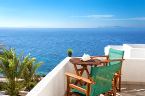 A wooden table with a white napkin and a potted plant on a balcony overlooking the sea.