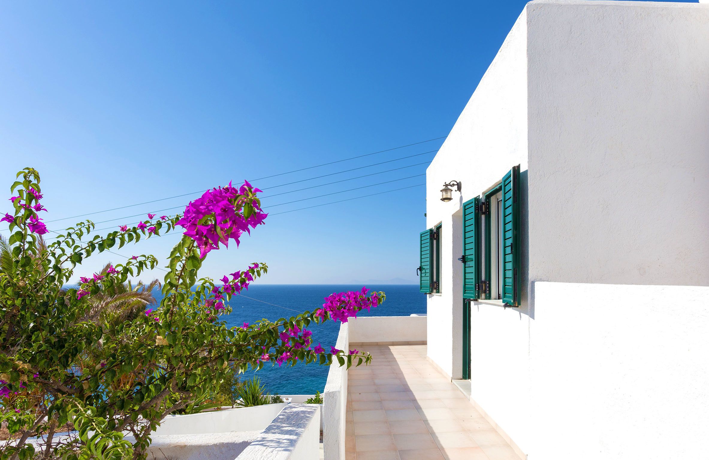 A white building with green shutters and a balcony overlooking the sea.