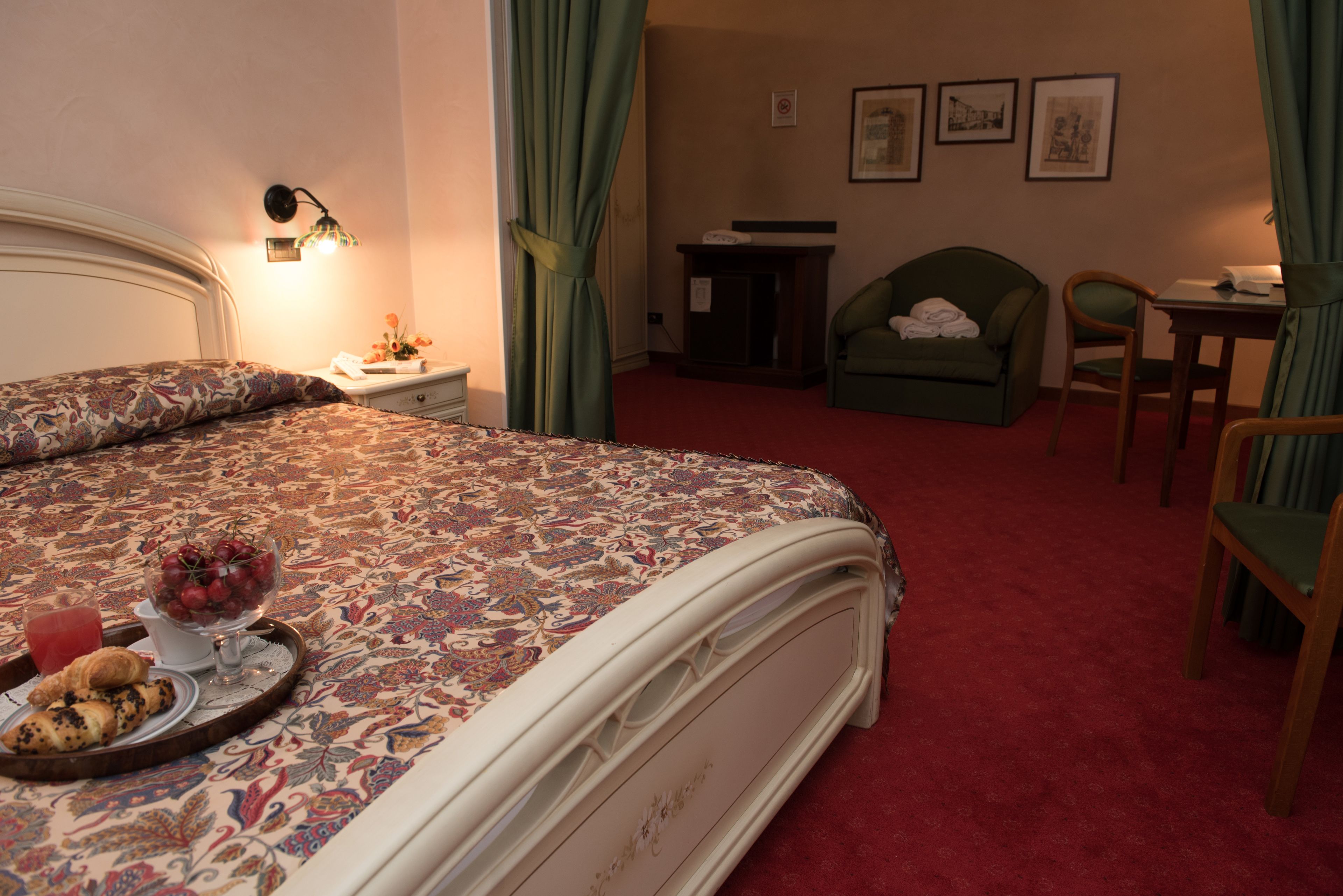 Ein Hotelzimmer mit einem großen Bett, einem Nachttisch mit Lampe, einem Sessel, einem Schreibtisch und einem kleinen Tisch mit einer Speisewagenaufsatz.