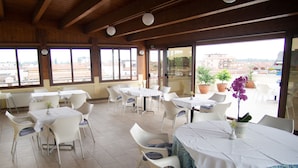 A restaurant with white tables and chairs, large windows, and potted plants. - Hotel Tessarin (Taglio di Po)