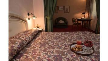 Un dormitorio con cama, mesita de noche, silla, mesa y una ventana pequeña con cortinas.