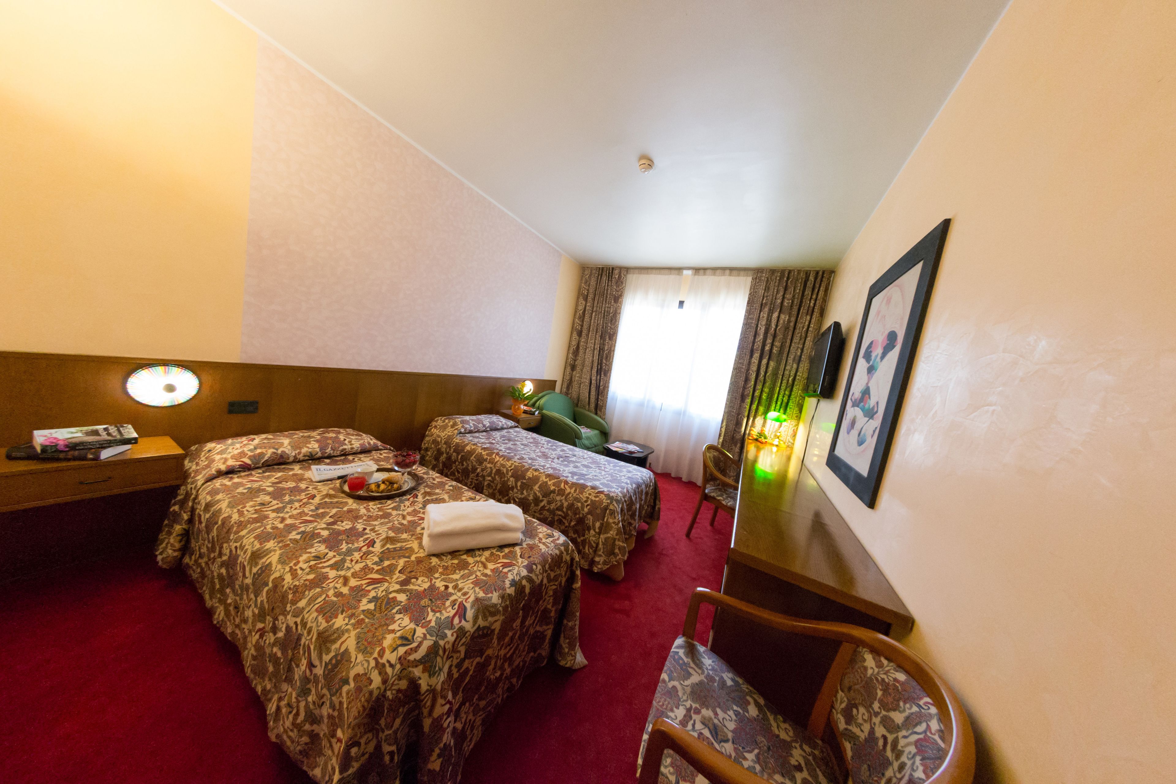 A hotel room with two beds, a desk, a chair, and a window with curtains.