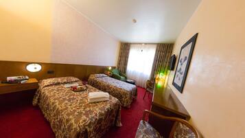 A hotel room with two beds, a desk, a chair, and a window with curtains.