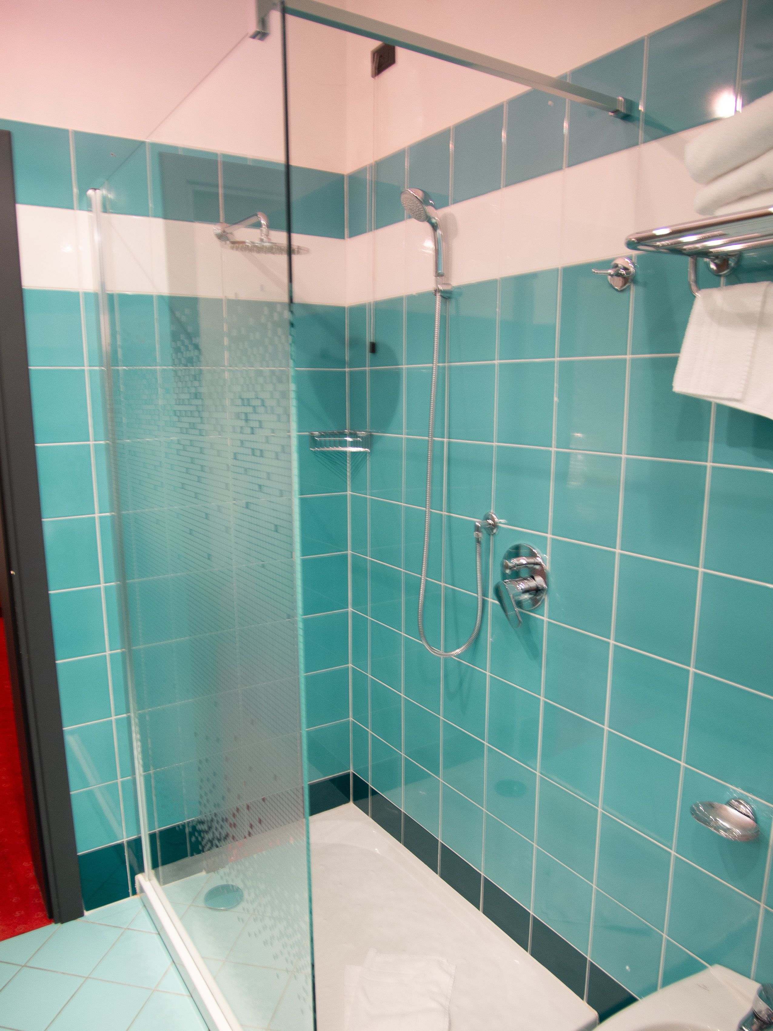Una cabina doccia in vetro con soffione a mano e rubinetto a parete.