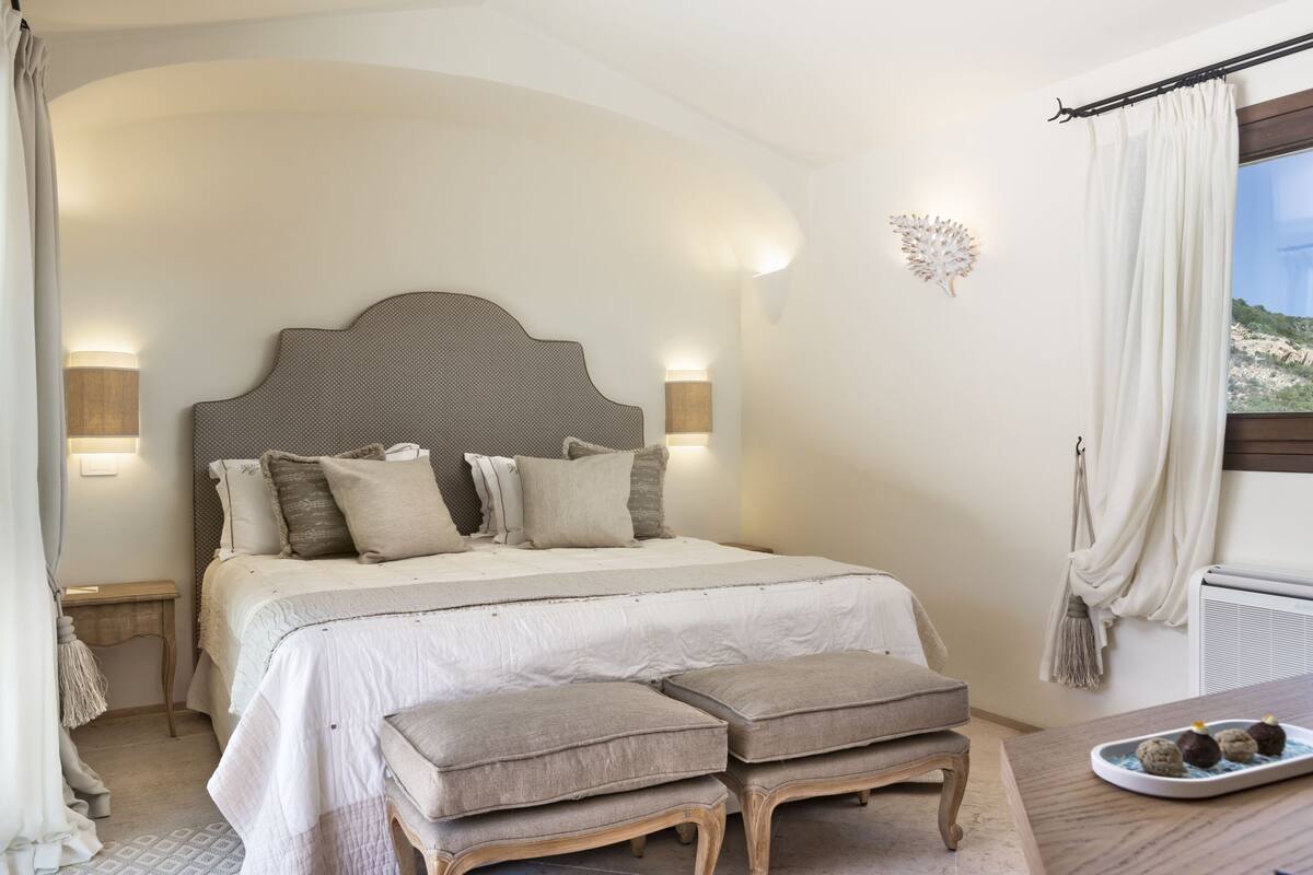 Een slaapkamer met een groot bed, bedlampen, een nachtkastje en uitzicht op de omgeving.