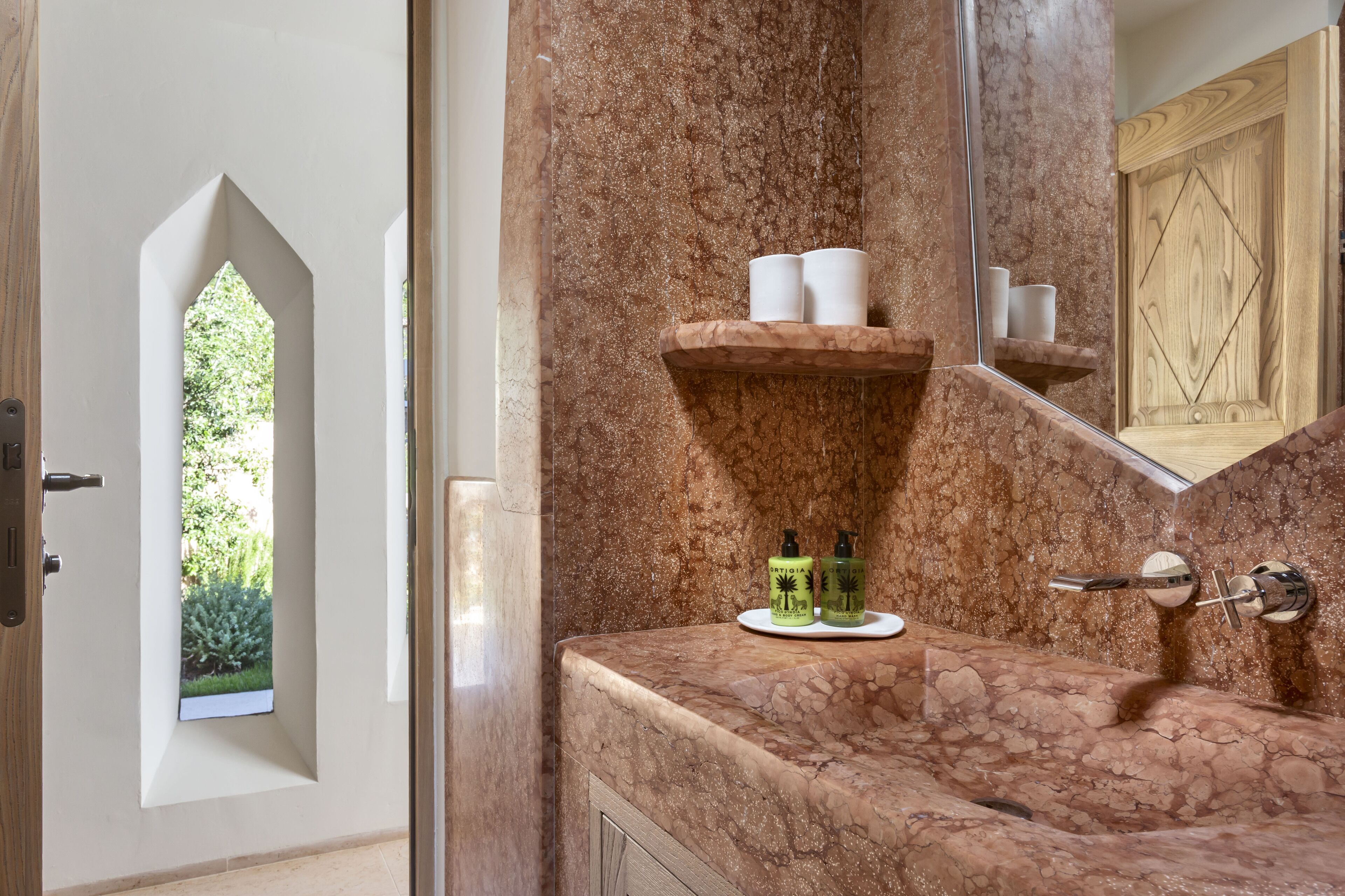 Ein Badezimmer mit Marmorwaschbecken, einem Ablagebereich für Toilettenartikel und einem Fenster mit Blick auf Grünflächen.