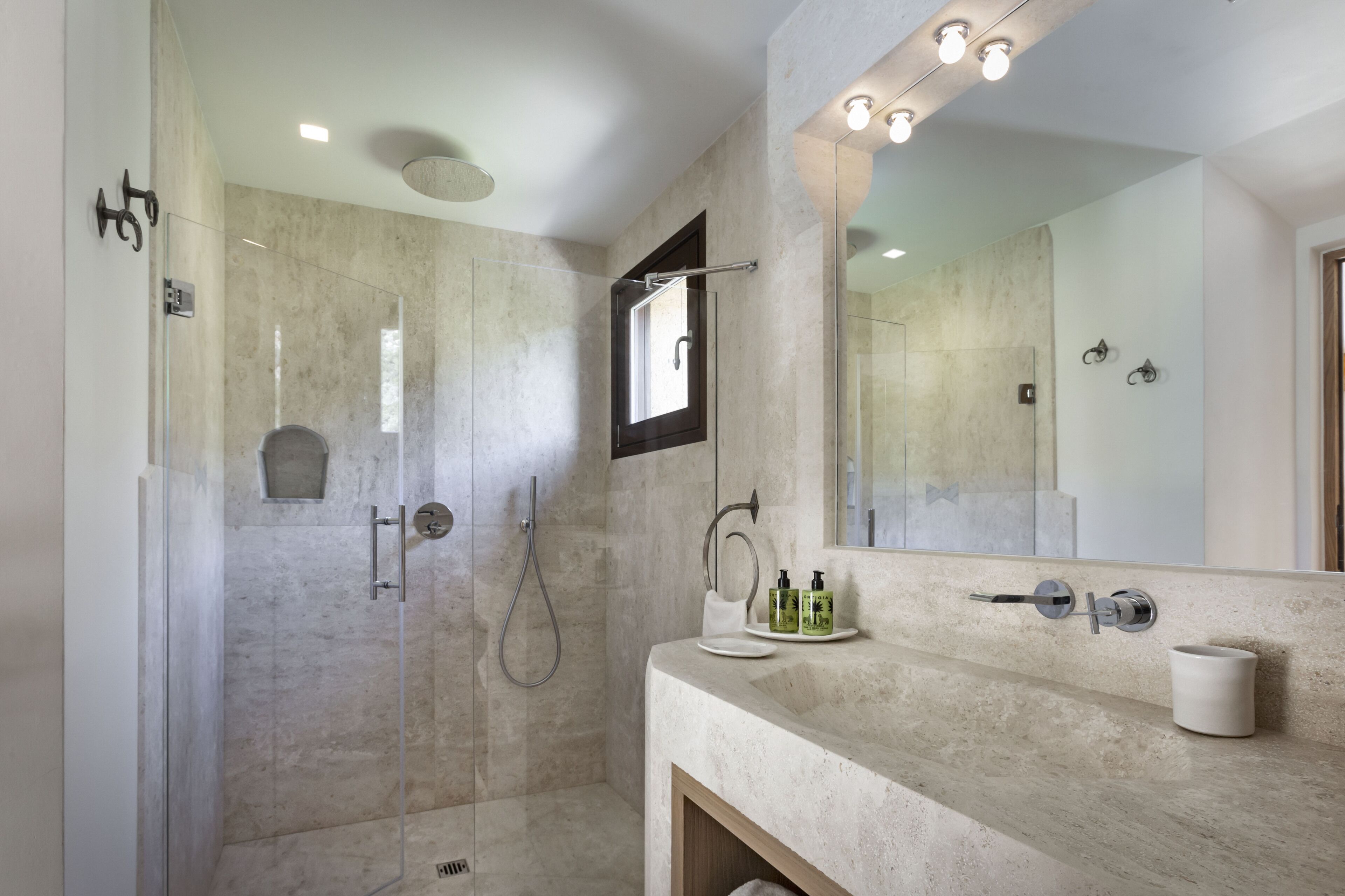 Un bany modern amb dutxa de vidre, un lavabo de marbre i un mirall gran.