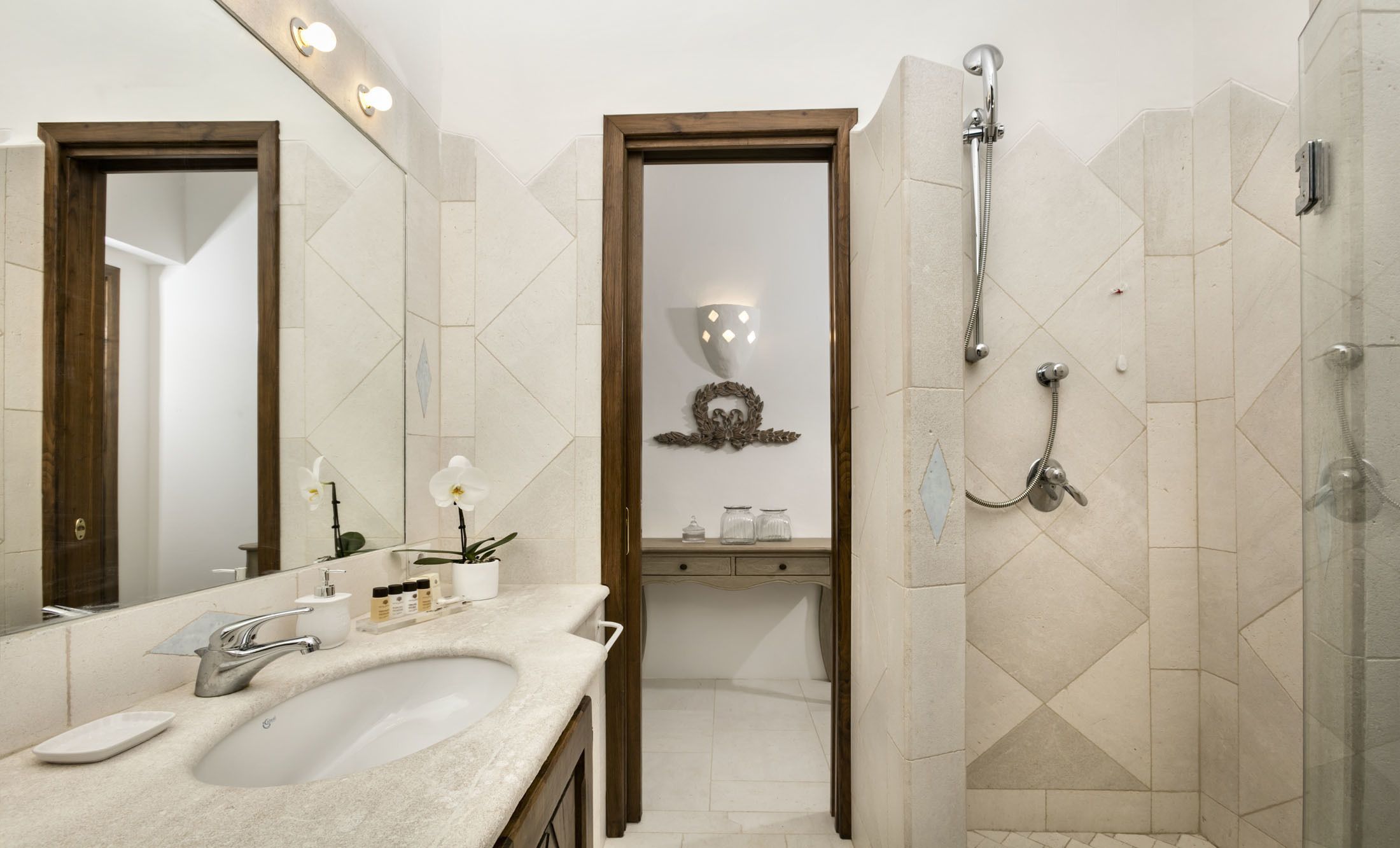 A bathroom with a large mirror, a sink, a shower, and a vanity with a mirror.