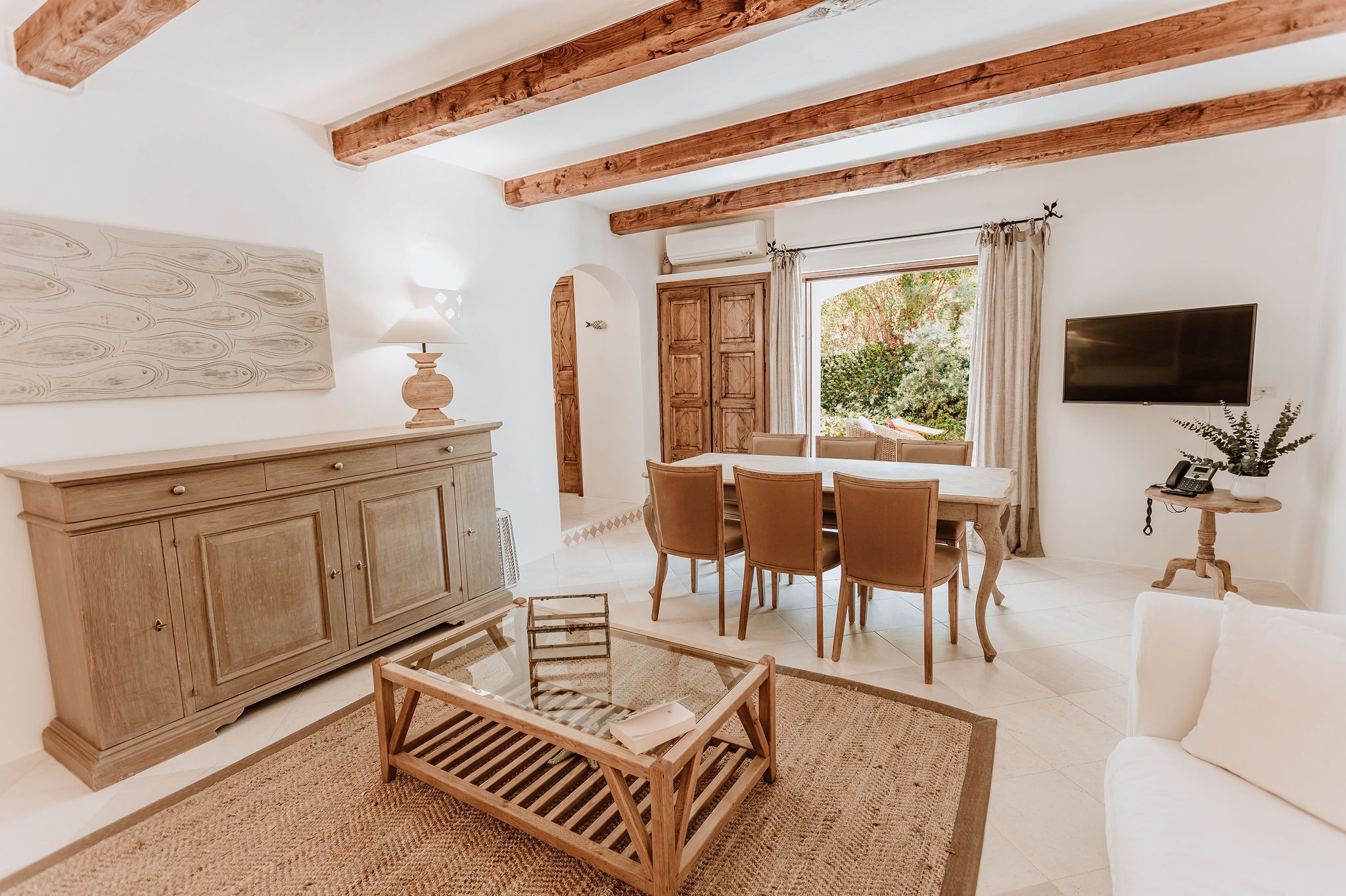 A spacious living room with a wooden dining table, white sofas, and a large window.