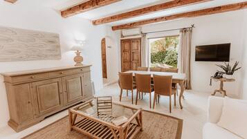 A spacious living room with a wooden dining table, white sofas, and a large window.