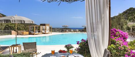 A poolside area with a table set for breakfast, lounge chairs, and umbrellas.
