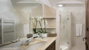 A bathroom with a sink, mirror, white towels, a shower, and orchids.