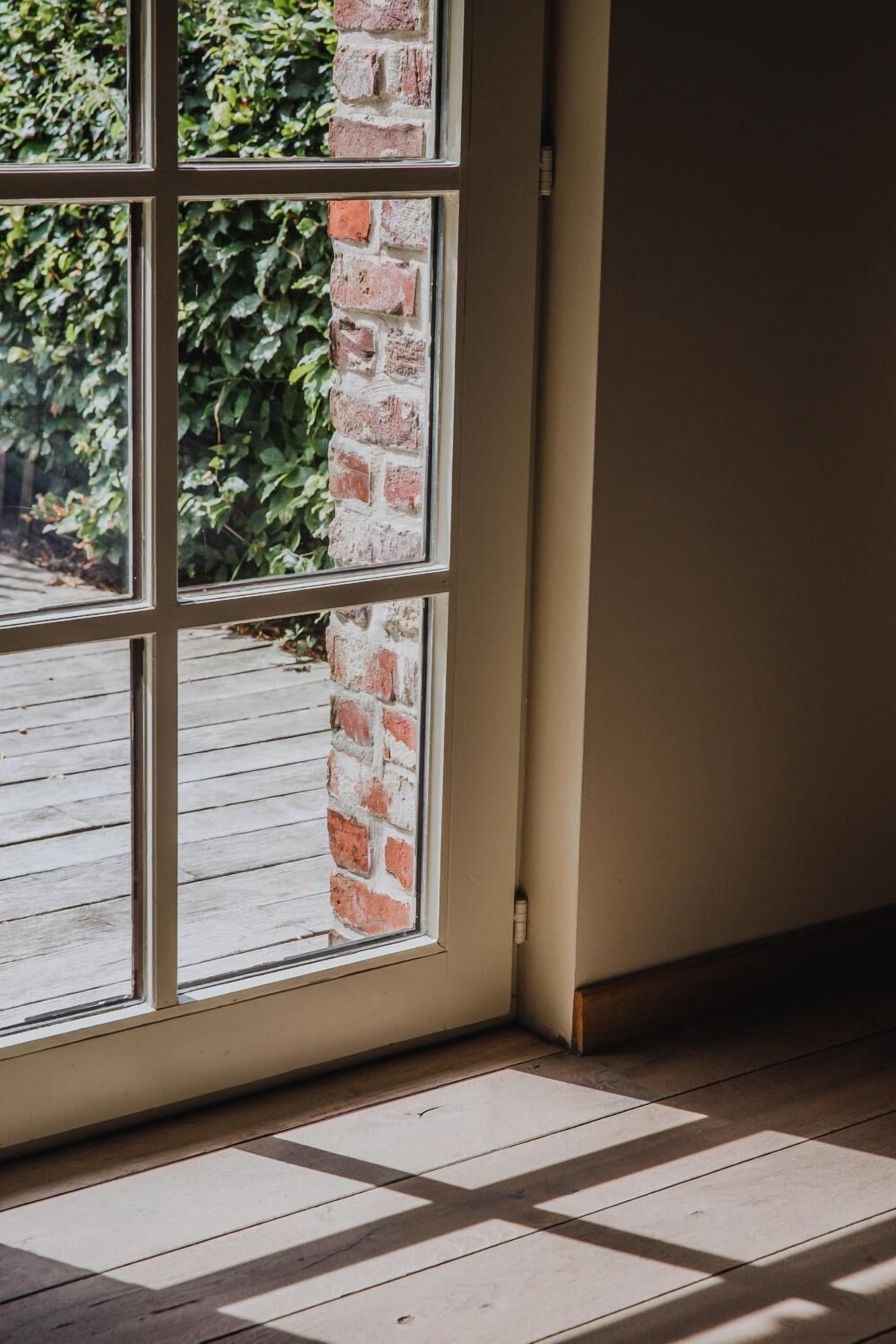A corner of a room with a large window, a brick wall, and a wooden floor.
