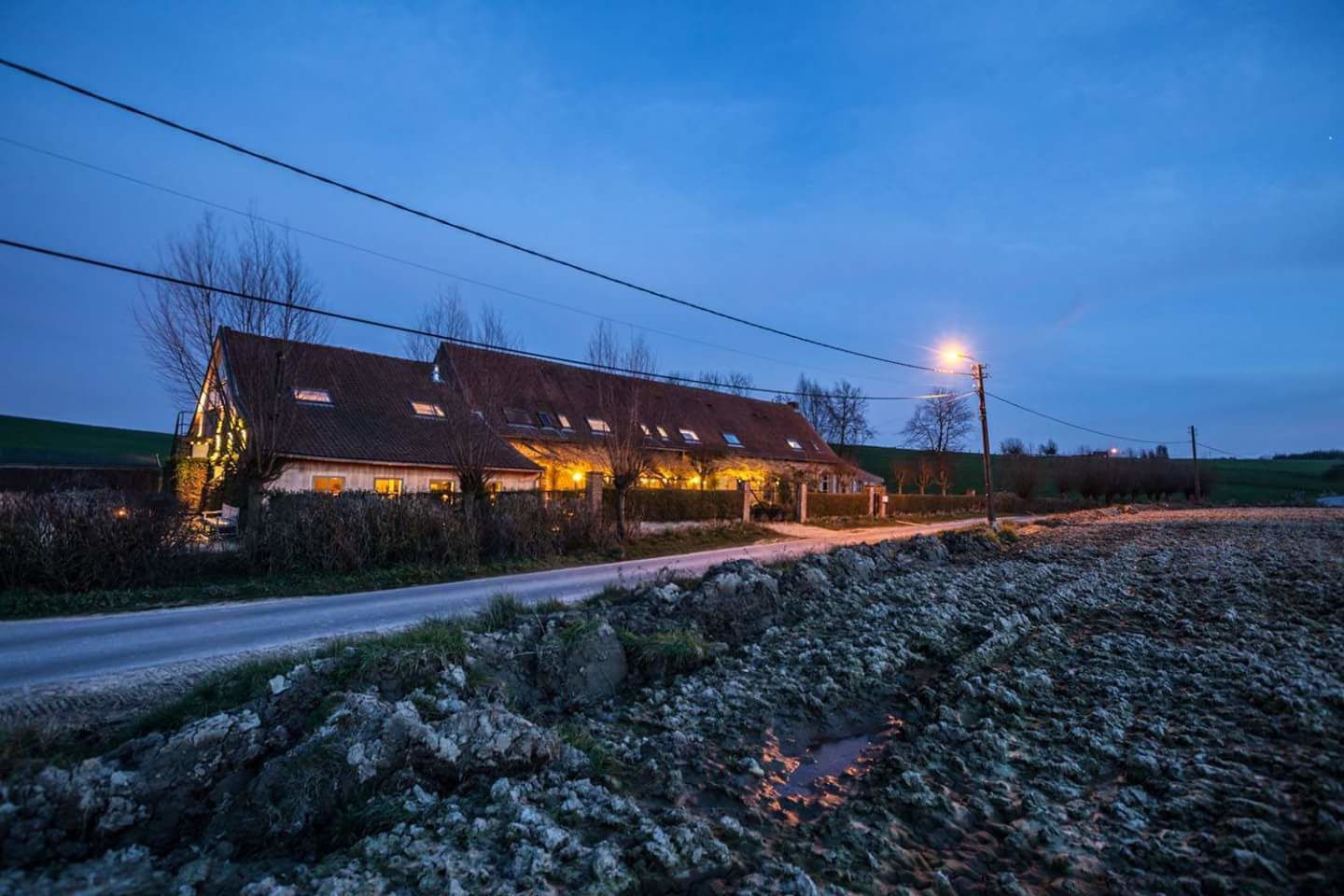 A rural house with a sloped roof, multiple windows, and a lit exterior at dusk.