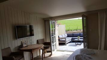 Een hotelkamer met een bed, een televisie, een eettafel met stoelen en uitzicht op een terras.