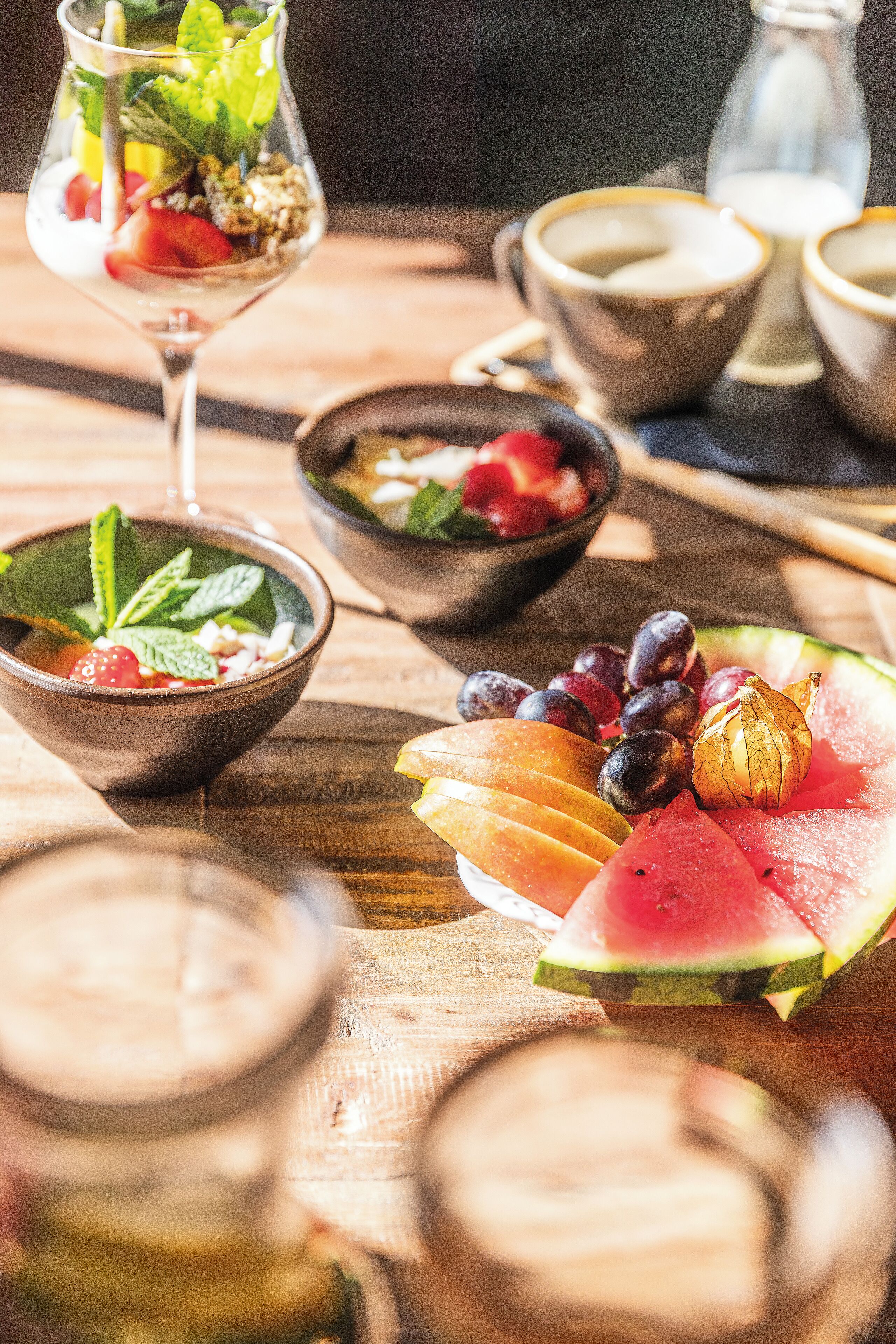 A table with various food items and drinks, including bowls of fruit, a glass of a layered drink, and a bottle of milk.